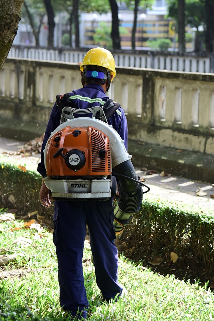 Worker using a leaf blower in a park, wearing safety gear.